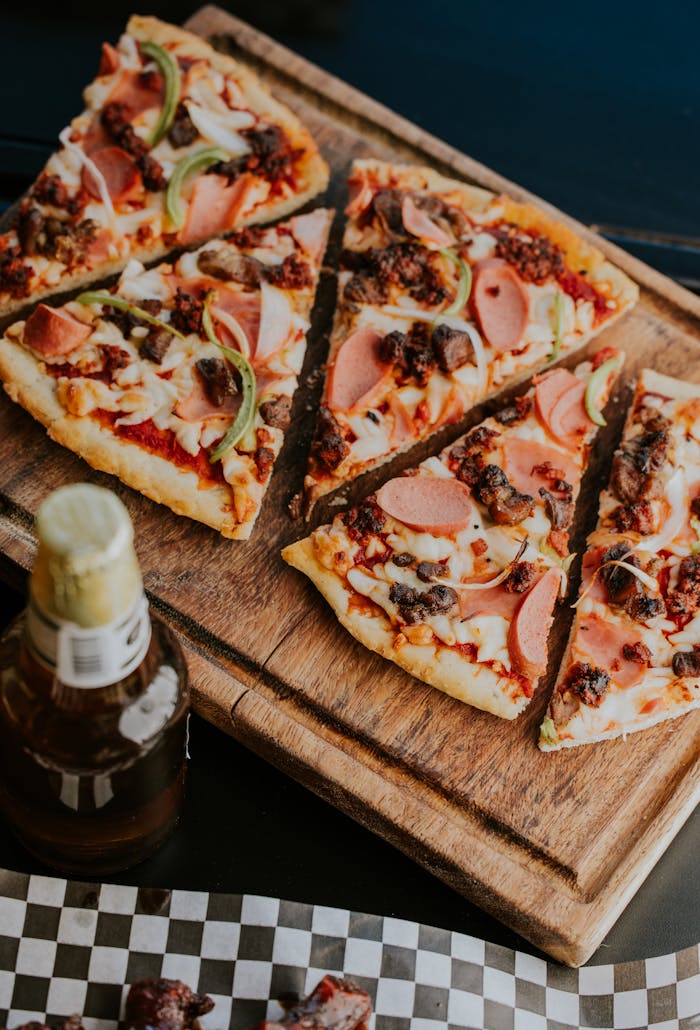 Close-up of gourmet pizza slices on a wooden board with fresh toppings and a bottle of beverage